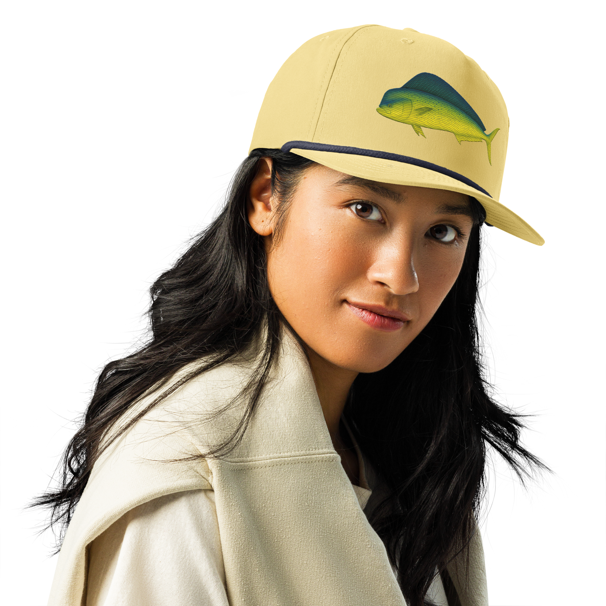 A person with long dark hair wears a light jacket and the tan Prop and Hook Mahi-Mahi Rope Hat, which features a fish image on the front, looking at the camera against a black background.